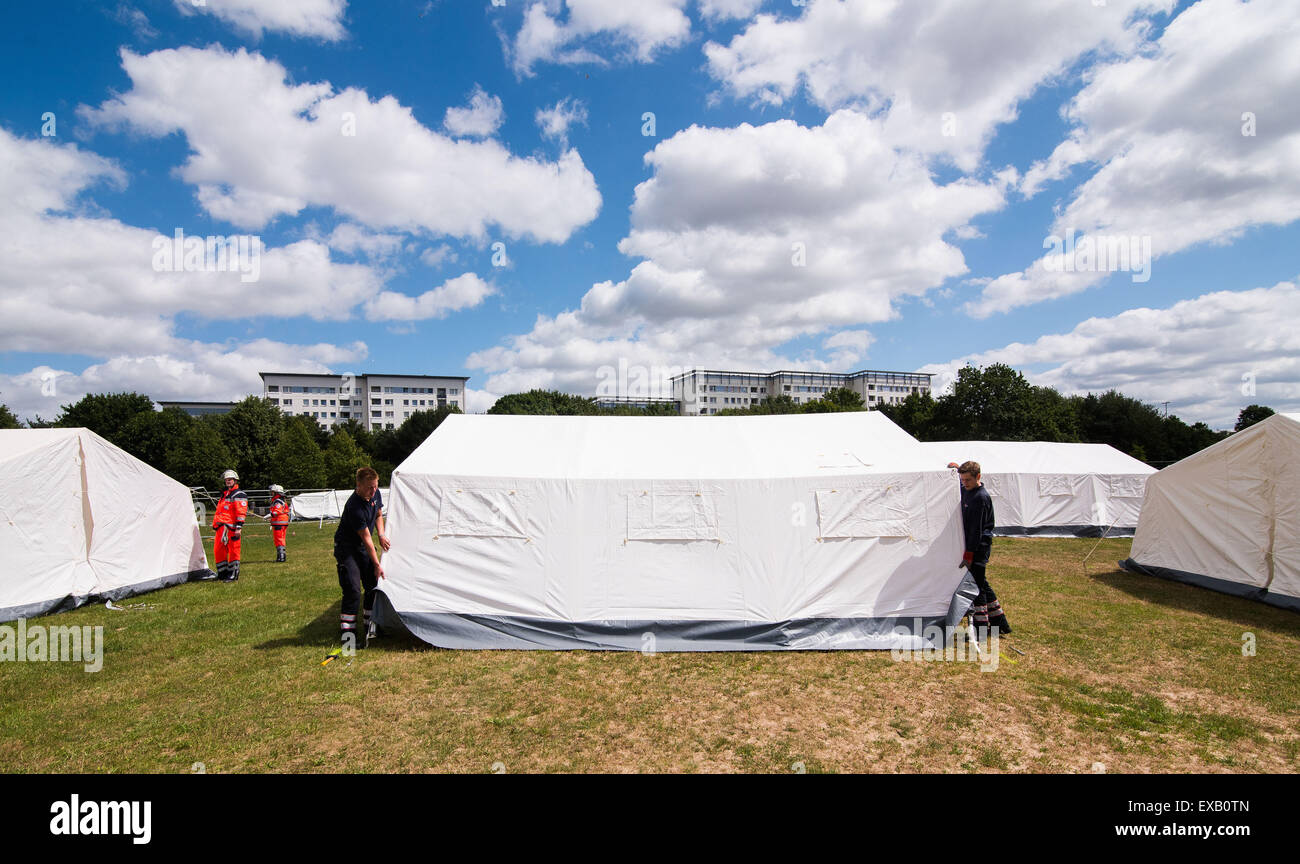 Helpers from the German Red Cross (Deutsches Rotes Kreuz) carry a tent at a new refugee accommodation centre in Hamburg, Germany, 10 July 2015. The city of Hamburg have been forced to take emergency measures due to the increasing number of incoming refugees. in the Jenfeld district, more than 800 refugees are now supposed to be housed in tents. PHOTO: DANIEL BOCKWOLDT/DPA Stock Photo