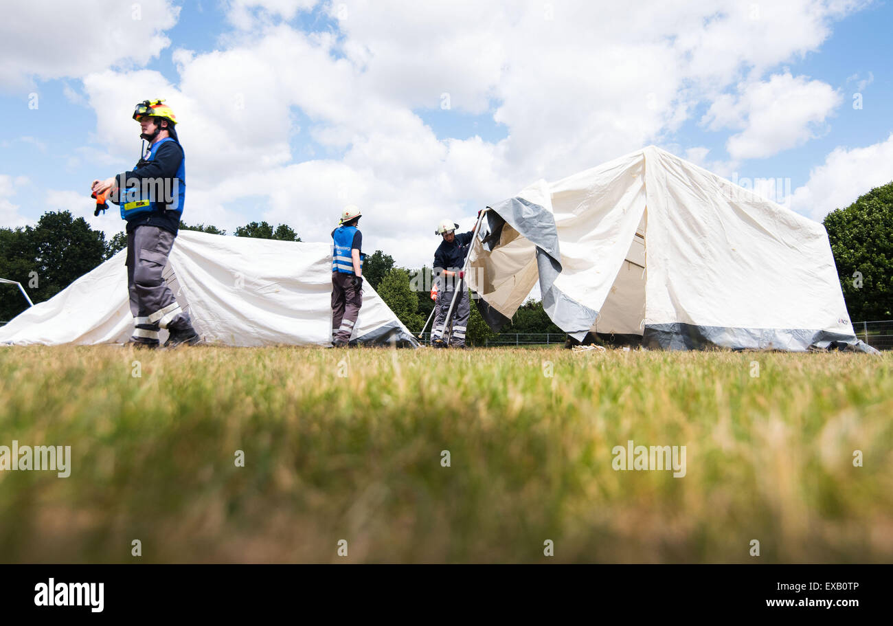 Helpers from the German Red Cross (Deutsches Rotes Kreuz) set up a tent at a new refugee accommodation centre in Hamburg, Germany, 10 July 2015. The city of Hamburg have been forced to take emergency measures due to the increasing number of incoming refugees. in the Jenfeld district, more than 800 refugees are now supposed to be housed in tents. PHOTO: DANIEL BOCKWOLDT/DPA Stock Photo