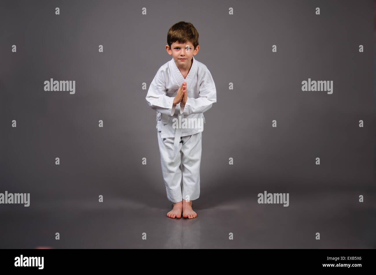 Karate boy in bowing pose wearing white kimono, on a gray background
