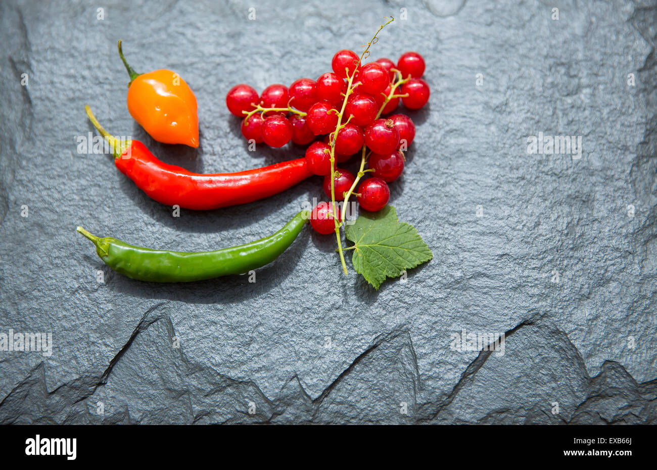 Redcurrants and chillies on slate platter. Stock Photo
