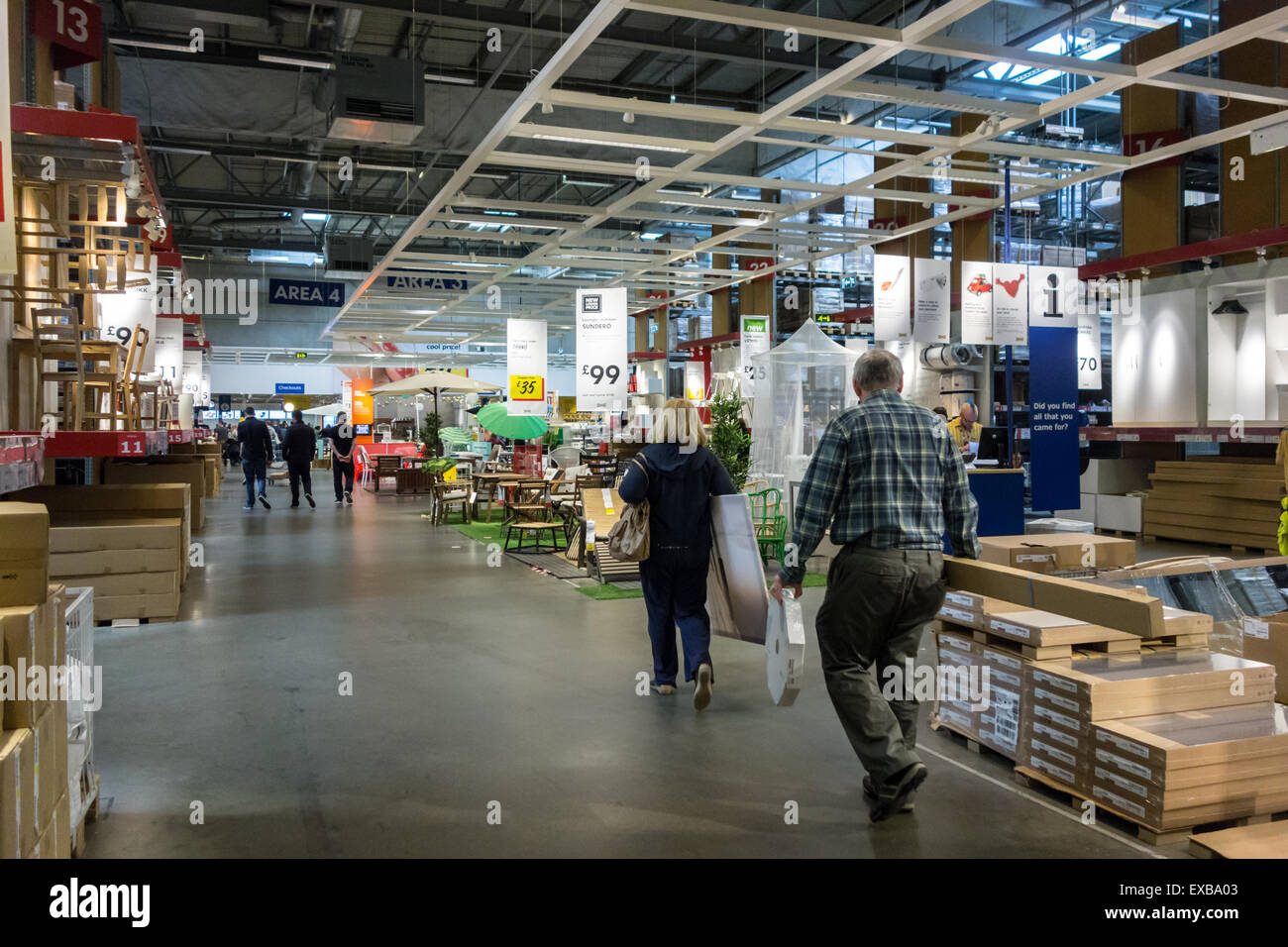 middle-aged couple carrying goods through Ikea warehouse towards the checkouts - Ikea, Braehead, Glasgow, Scotland, UK Stock Photo