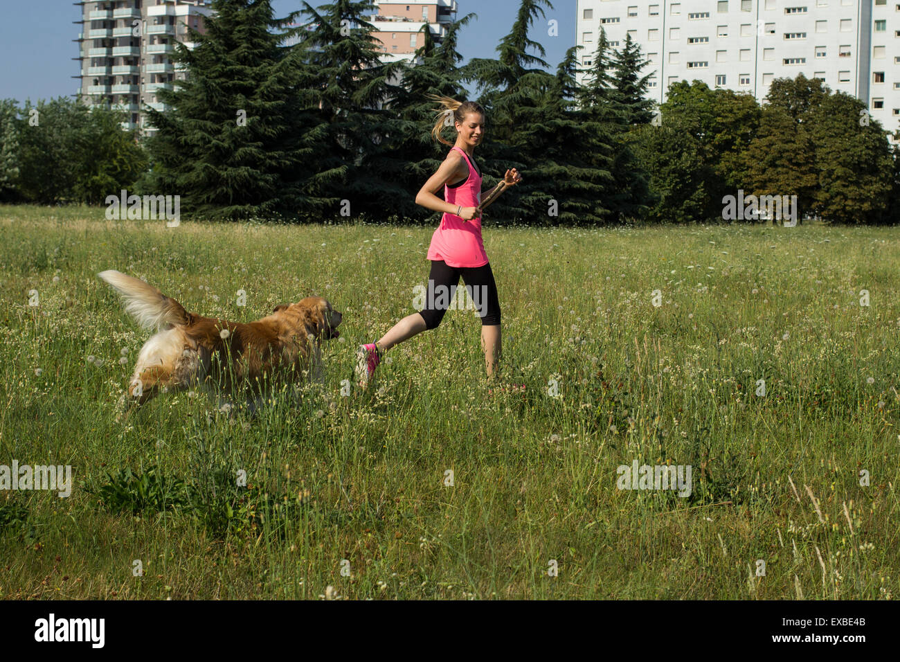 Blonde girl running at the park with her dog Stock Photo