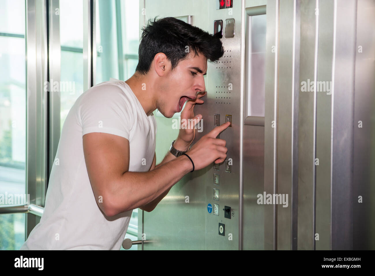 Scared young man desperate in stuck elevator screaming, looking very upset Stock Photo