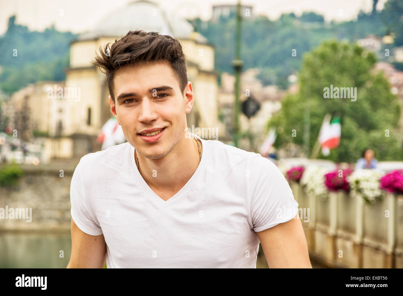 Handsome young man in white t-shirt outdoor in city setting, looking at camera, smiling Stock Photo