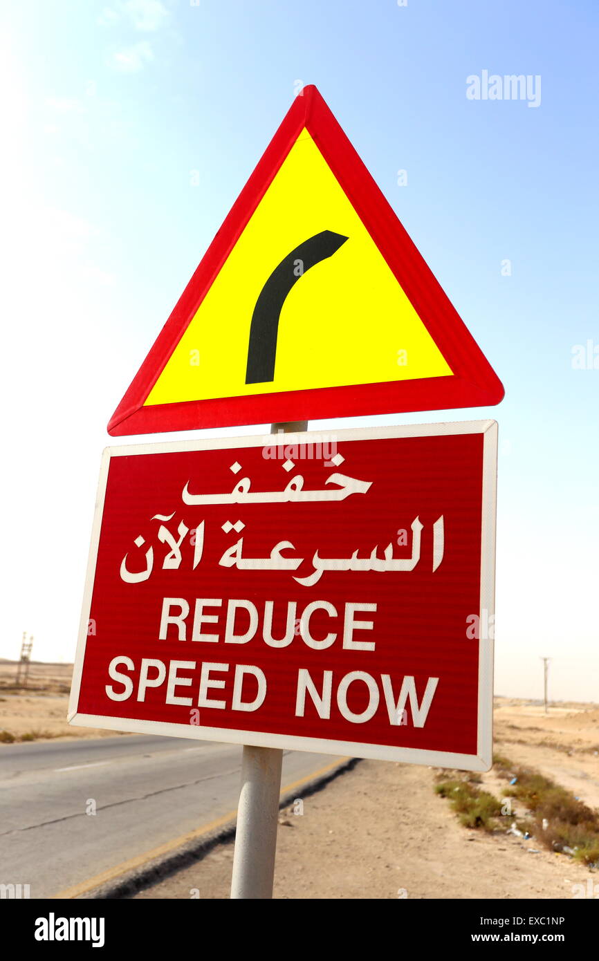 A road sign in Arabic and English telling motorists to reduce speed because of a bend in the road, Kingdom of Bahrain Stock Photo