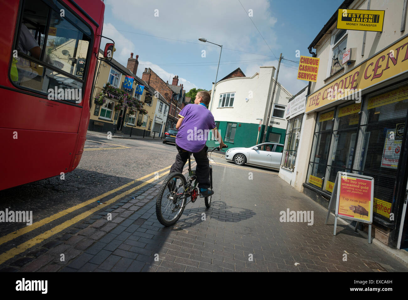 Boy on bike, cycling on and off pavement, avoiding bus and negotiating traffic in town centre, Willenhall, West Midlands, UK Stock Photo