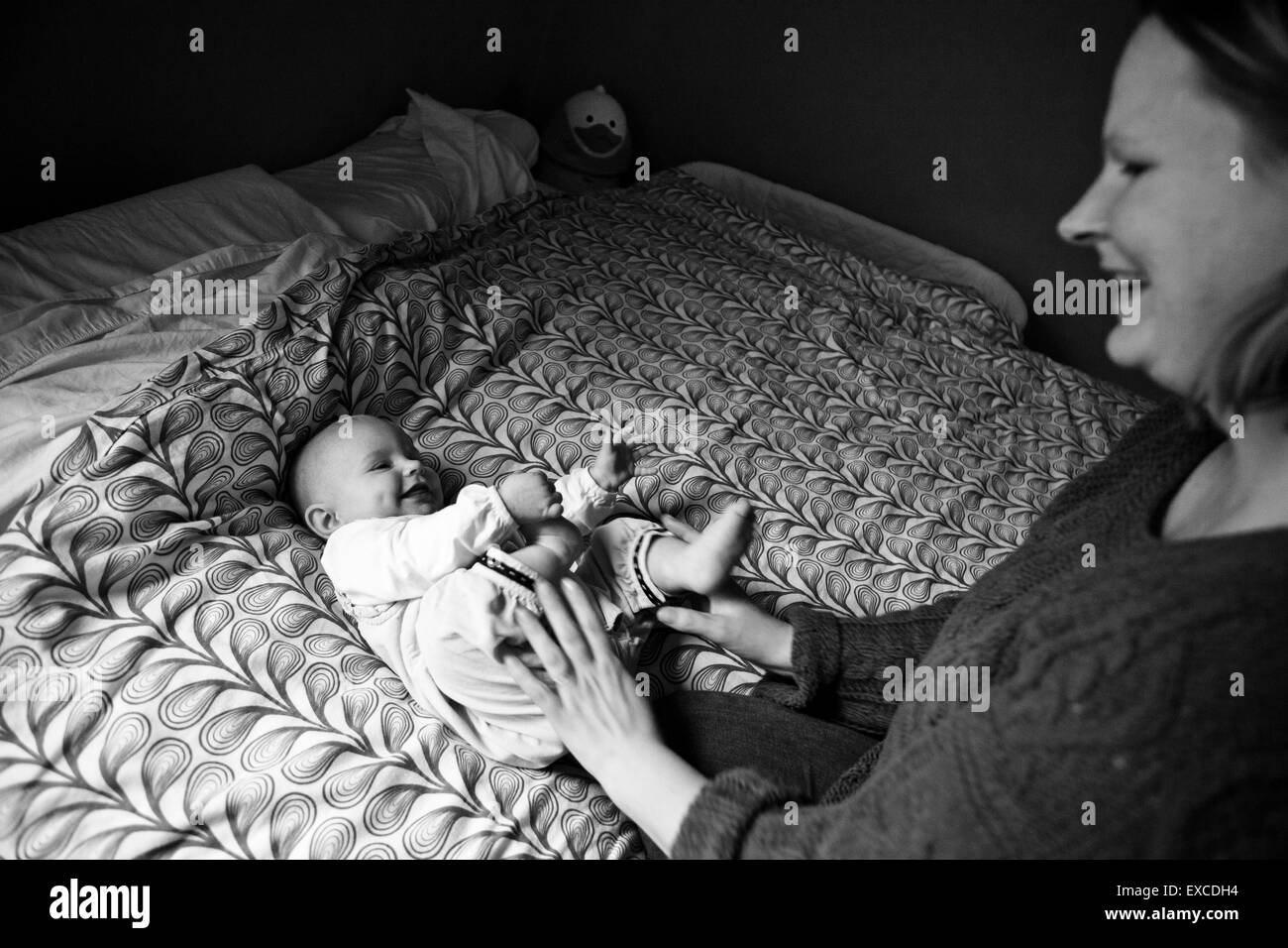 A mother plays with her little baby girl on a bed. Stock Photo