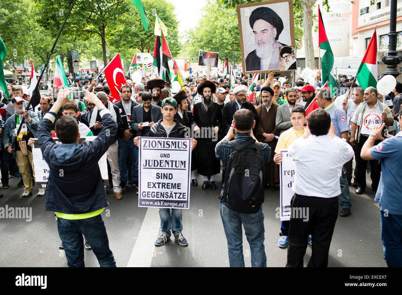 Berlin, Germany. 11th July, 2015. People march during a rally held in support of the Palestinian Territories and against zionism on occasion of the annual Quds Day in Berlin, Germany, 11 July 2015. A boy carries a sign that reads 'Zionismus und Judentum sind extreme Gegensaetze' (lit. zionism and judaism are extreme contradictions) as other participants hold up a picture of Ayatollah Khomeini. Anti-Israeli rallies are held in Iran on Quds Day. Photo: GREGOR FISCHER/dpa/Alamy Live News Stock Photo