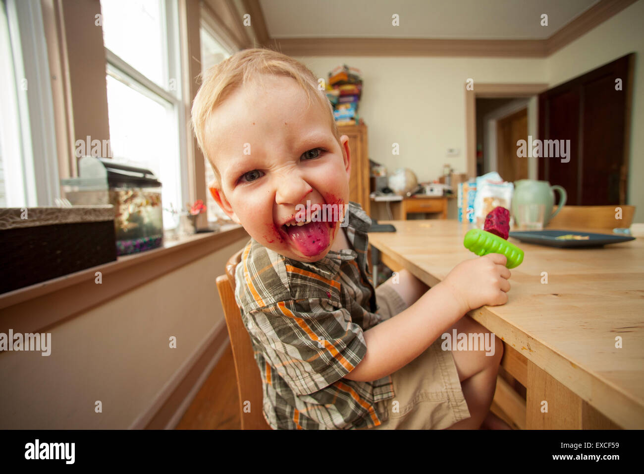 A young blond boy eating a popsicle with a messy face sticks his tongue out. Stock Photo