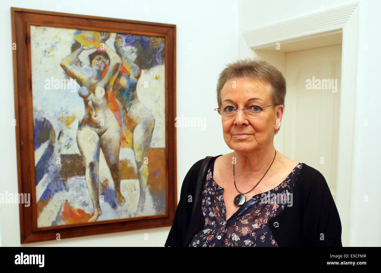 Leipzig, Germany. 11th July, 2015. Ingrid Sitte, widow of German painter Willi Sitte (1921-2013), poses in front of a painting entitled 'Laufende Akte' from 1962 in an exhibition at Galerie Schwind in Leipzig, Germany, 11 July 2015. The exhibition, which will run until 05 September 2015, showcases 19 works Willi Sitte created between 1951 and 2001. PHOTO: SEBASTIAN WILLNOW/dpa/Alamy Live News Stock Photo