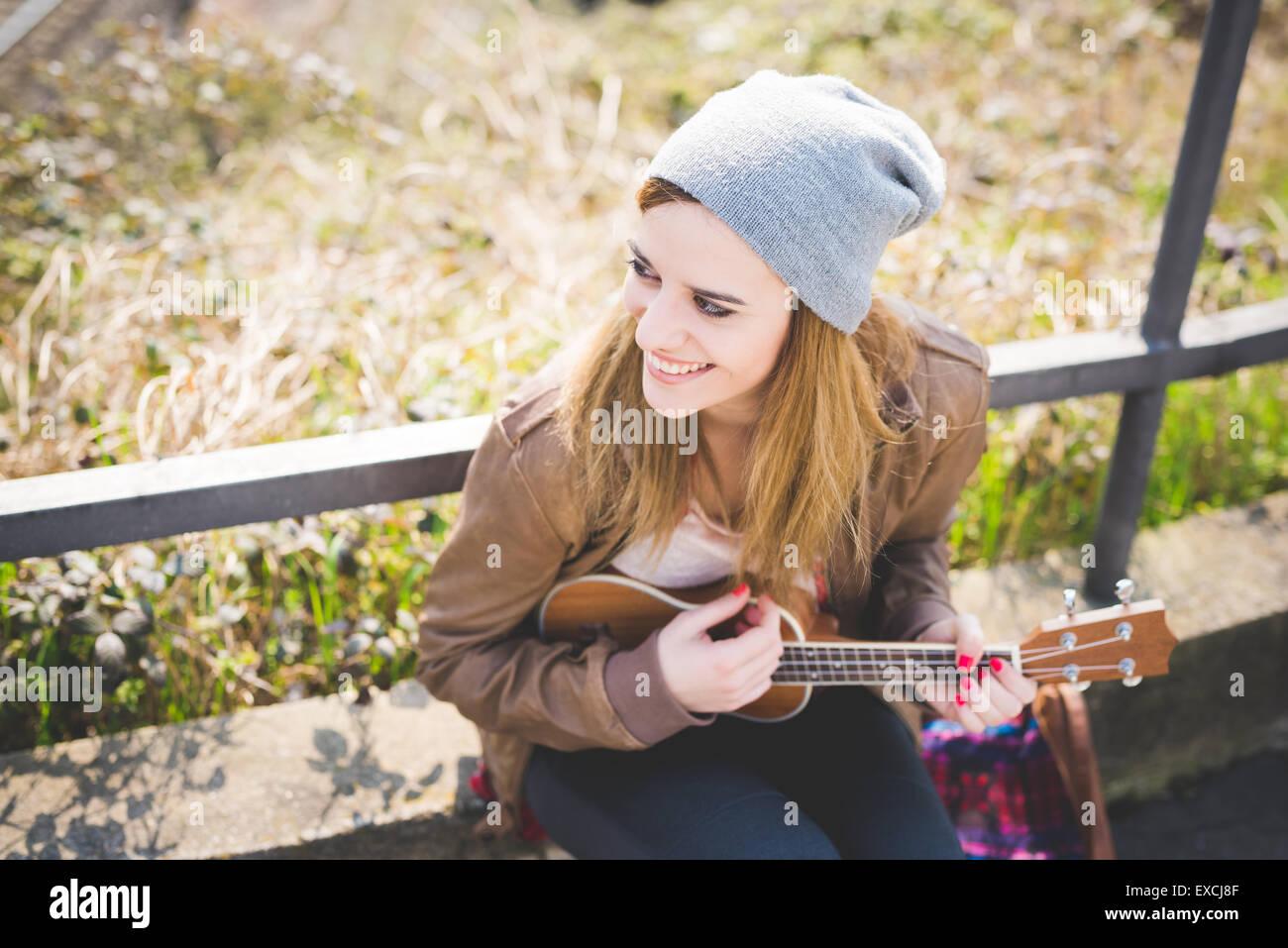 young beautiful blonde hipster woman in the city playing ukulele Stock