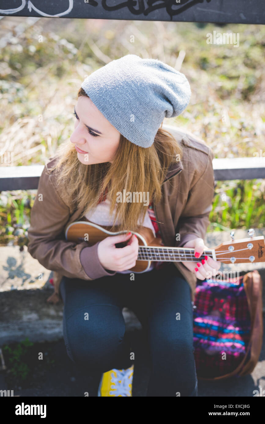 young beautiful blonde hipster woman in the city playing ukulele Stock