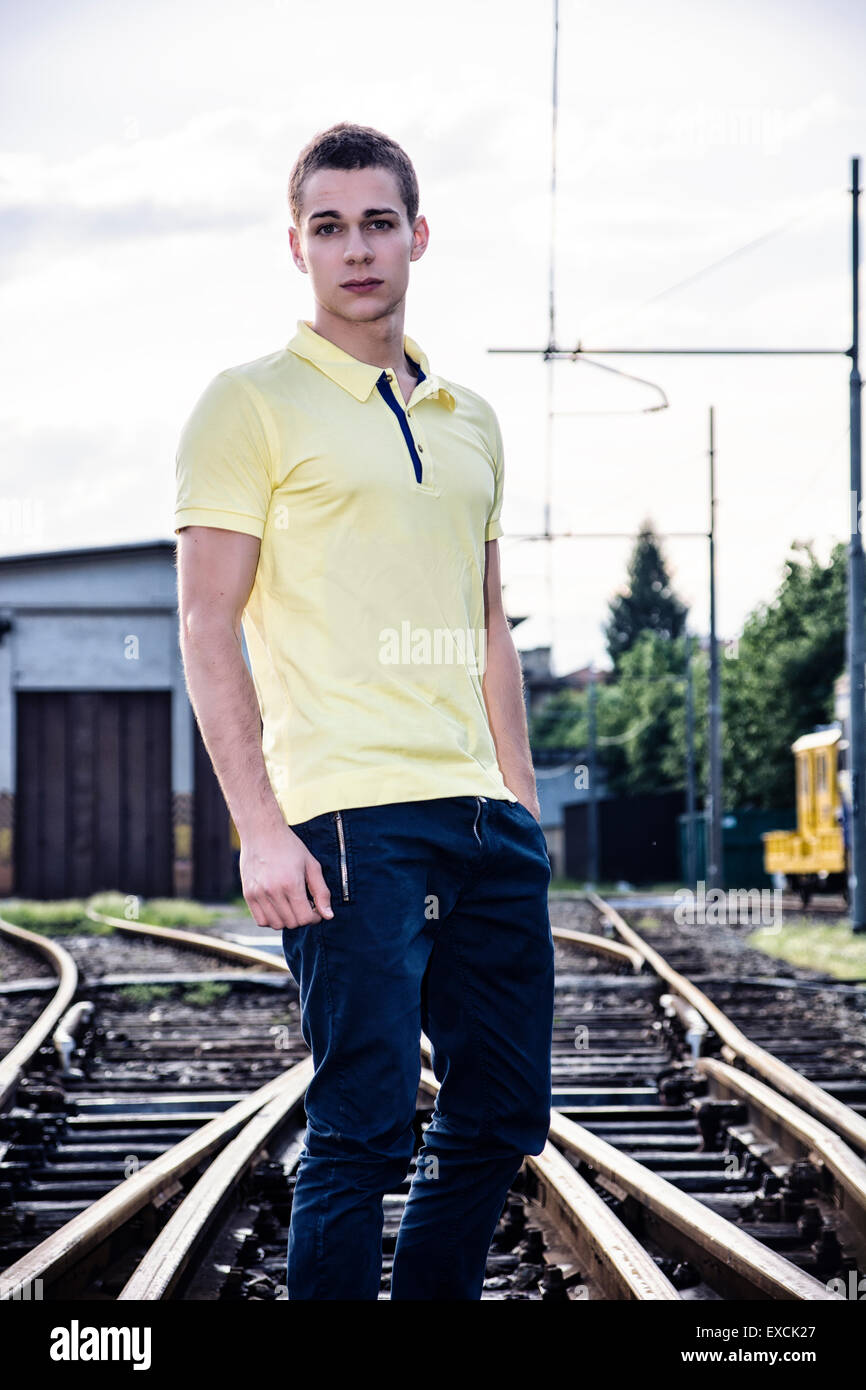 Attractive young man standing on railroad, wearing yellow polo shirt and  jeans, looking at camera Stock Photo - Alamy
