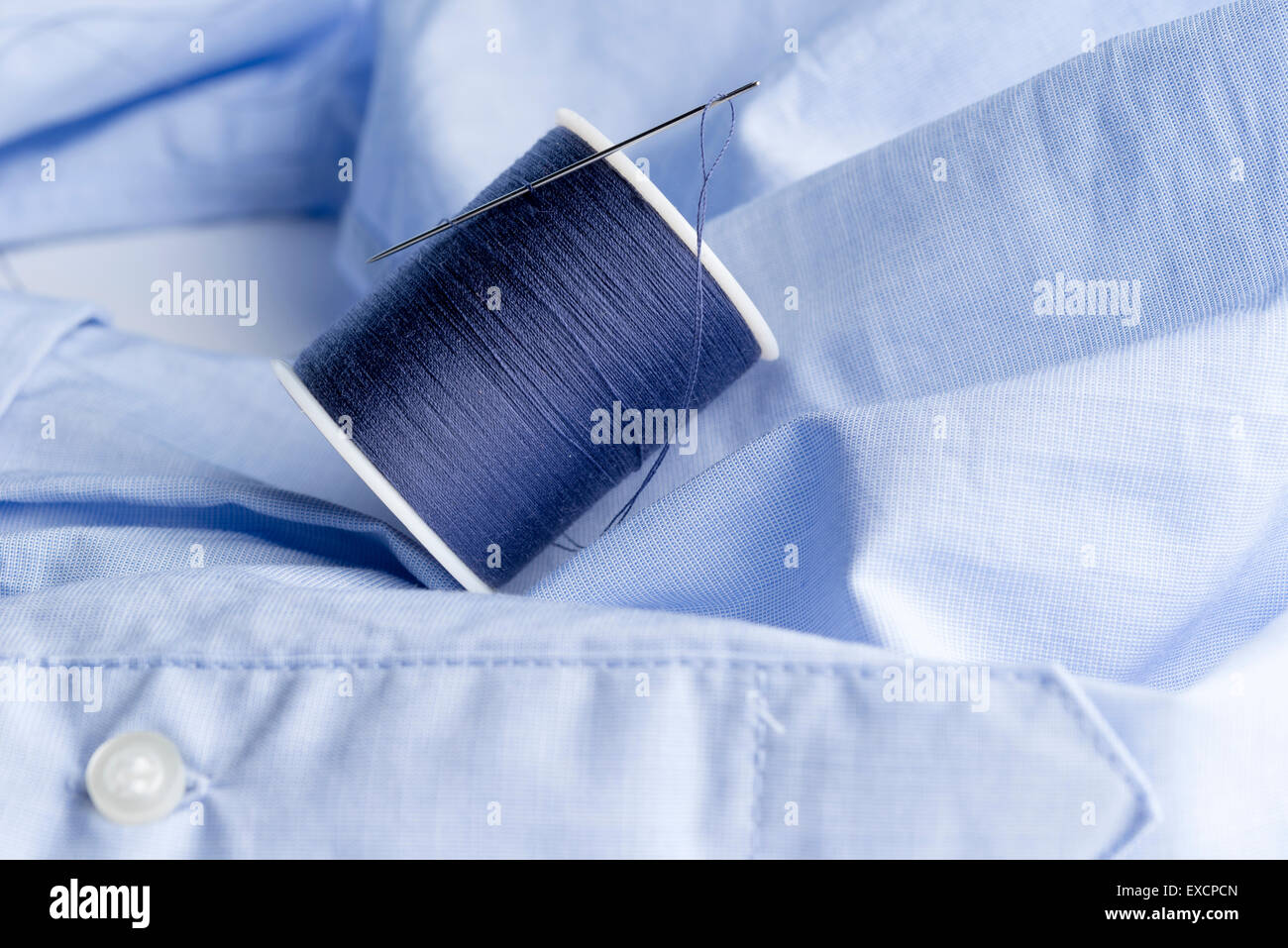 spool of navy blue silk cotton sewing tread  and a needle laying on light blue material. Stock Photo