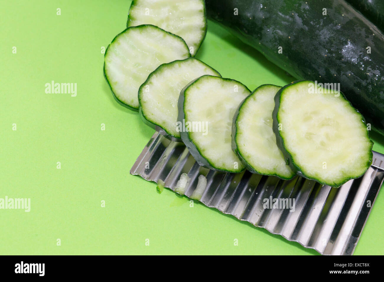 Chopped cucamber ordered on top of the vegetable chopper on green background Stock Photo