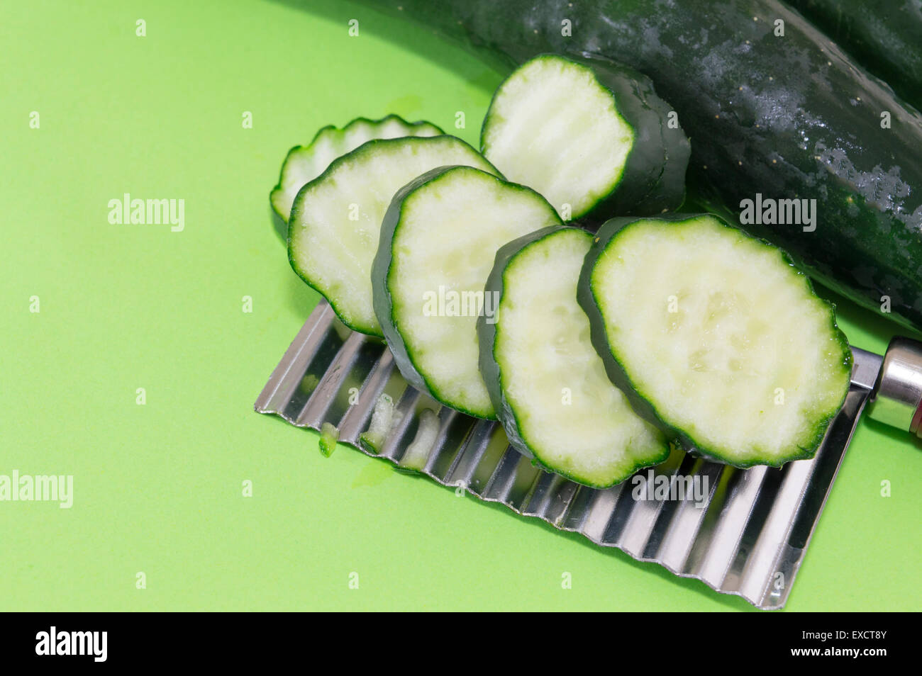 Chopped cucamber ordered on top of the vegetable chopper on green background Stock Photo