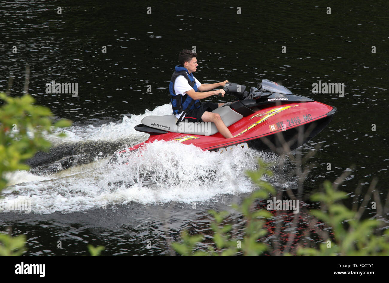 Teenage boy riding a red Sea Doo Bombardier personal watercraft. Long Lake New York Adirondack State park Adirondacks USA US Stock Photo
