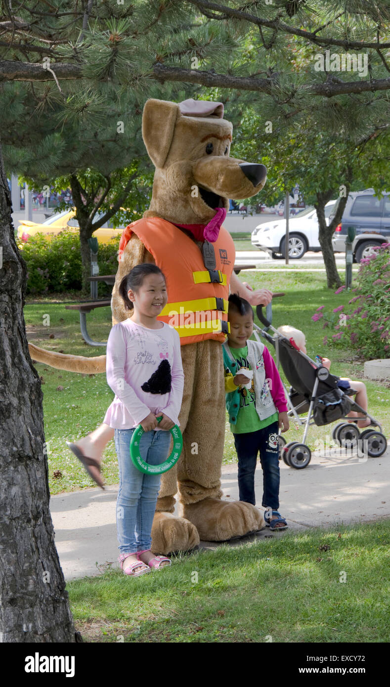 Manitowoc, Wisconsin. 11th July, 2015. Children pose for photo with Bobber the Water Safety Dog, US Army Corps of Engineers teaching mascot, at Manitowoc, Wisconsin Crazy Days street fair. Bobber appears at various summertime events to promote and present information on safe water recreation. Credit:  Jerome Wilson/Alamy Live News Stock Photo