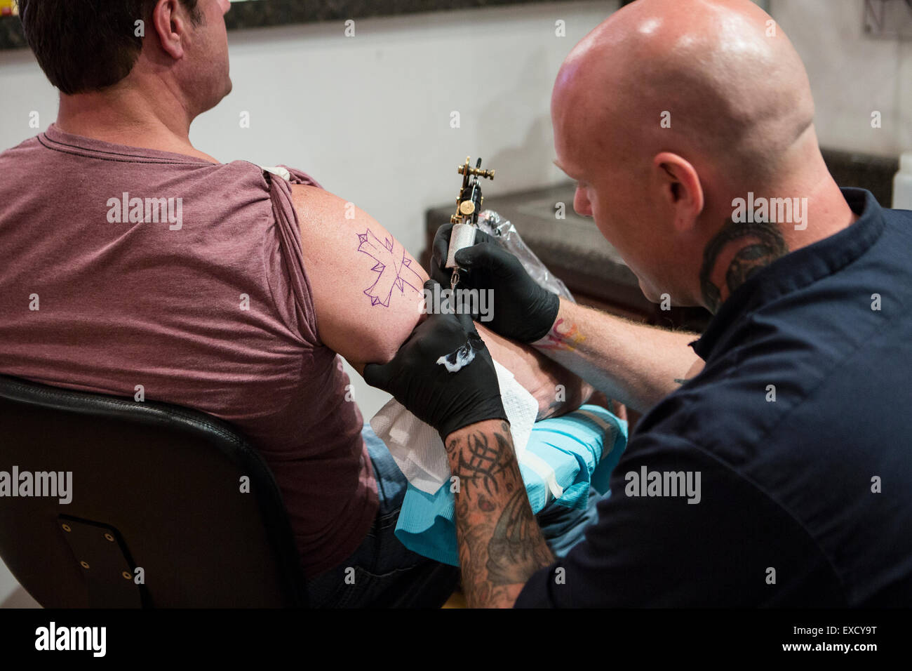 A tattoo artist giving a tattoo of a cross on a man's arm. Stock Photo