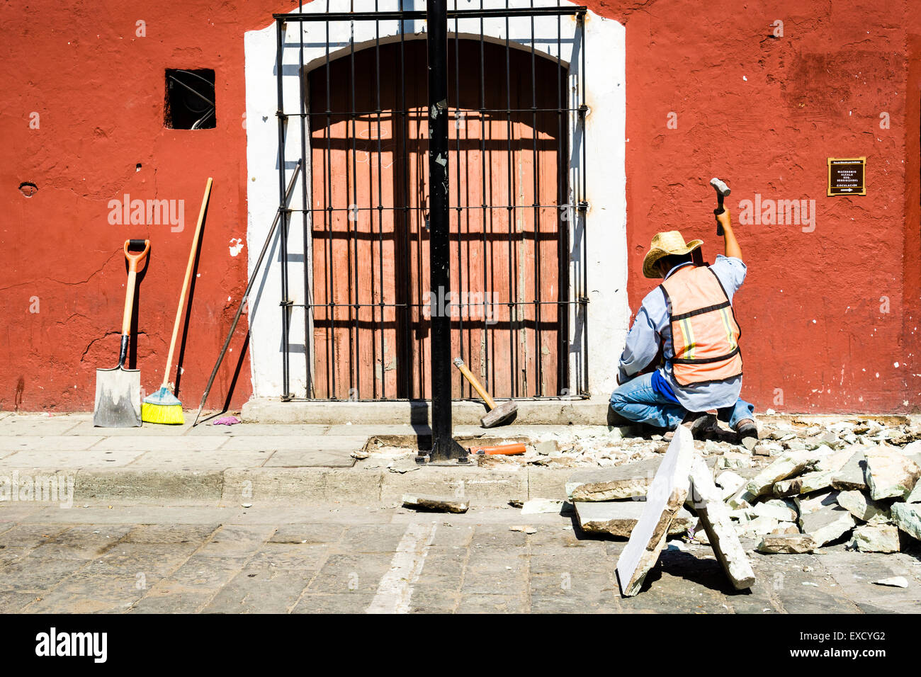 Construction worker swinging a hammer to tear up and repair stone sidewalk in the hot afternoon sun Stock Photo