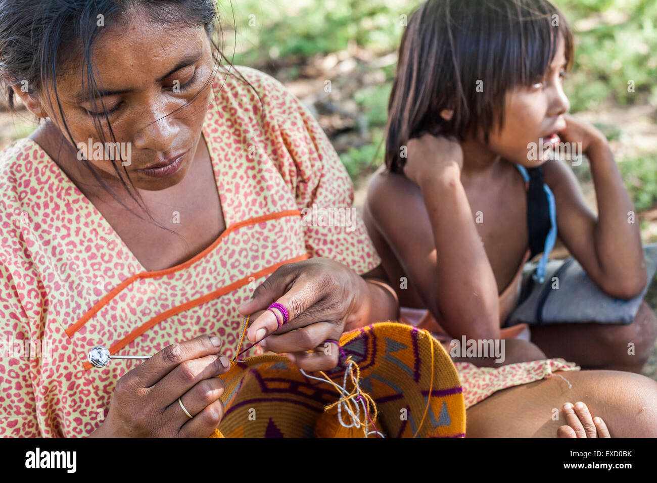 Young Wayuu woman and her children sitting outside while she knits in a 'rancheria', or traditional Wayuu settlement in La Guaji Stock Photo