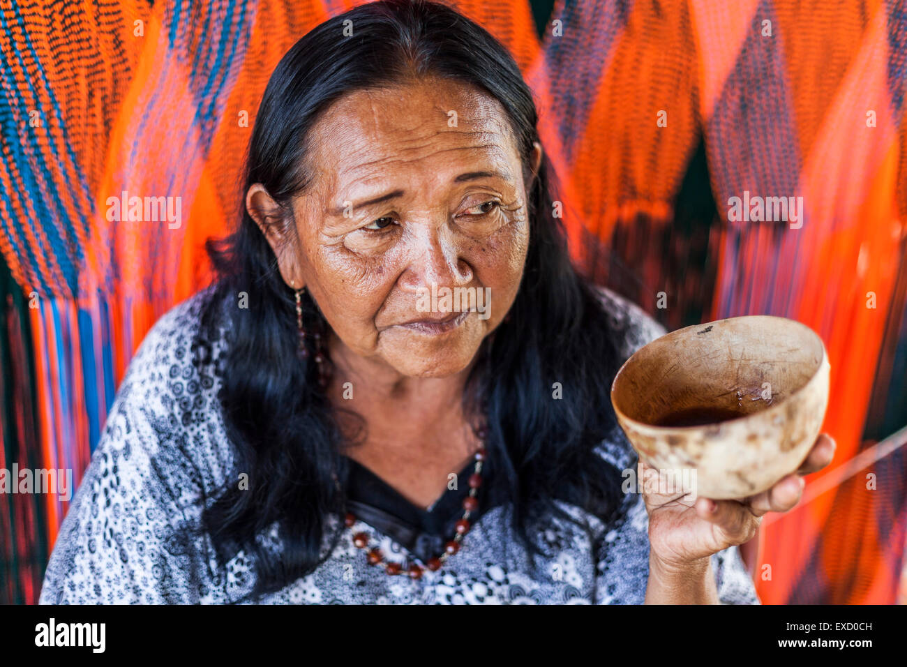 An elderly Wayuu woman drinking 'tinto' or sweet black coffee from a calabash cup in front of her loom.  Knitting, crocheting an Stock Photo
