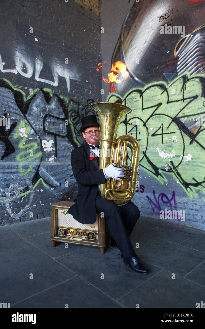 London street entertainer / performer: sitting on radiogram and playing a tuba. London busker UK. Stock Photo