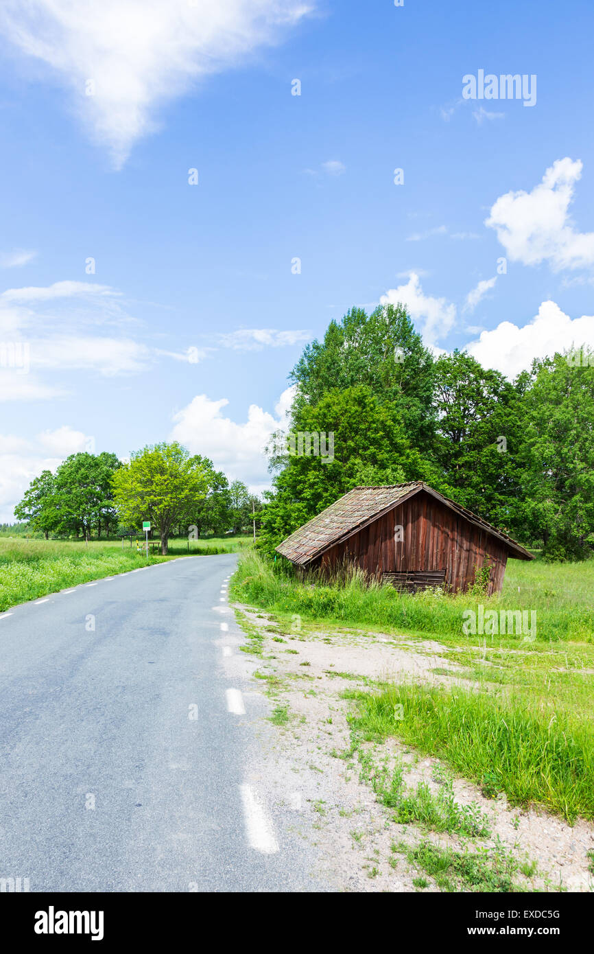 Old Worn Red Barn Near Road With a Blue Cloudy Sky Stock Photo