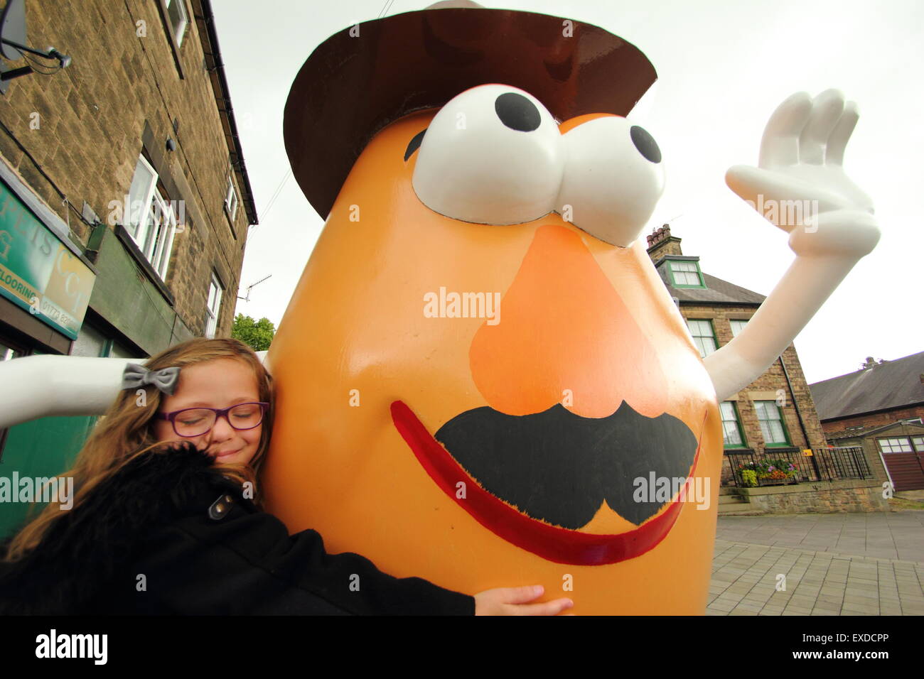 Belper, Derbyshire, UK. 12th July, 2015. Brii Matheson, 8,from Belper hugs a giant Mr Potato Head that has re-appeared in a Derbyshire town. The 7ft fibreglass statue was gifted to Belper in 2001 by its twin town, Pawtucket, Rhode Island, USA. After being dubbed a 'monstrosity' by some locals, the divisive character made national headlines. It was vandalised and banished. Now the spud has been spruced up by a local youth group and unveiled at Belper’s food festival today. Credit:  Deborah Vernon/Alamy Live News Stock Photo