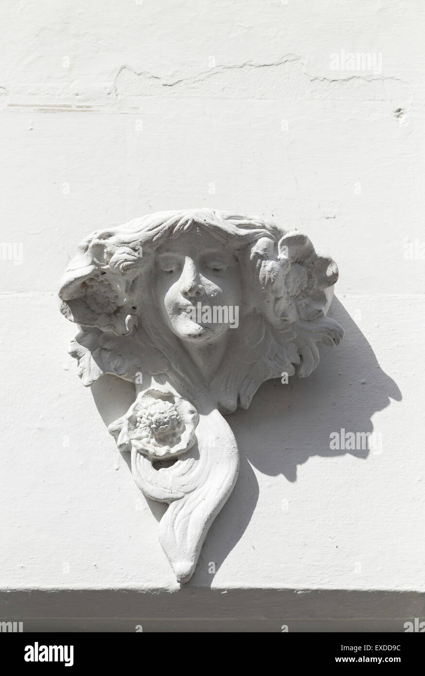 An Art Nouveau style wall sculpture of a beautiful woman's head in Polperro, Cornwall with sunshine casting a shadow across the white surface. Stock Photo