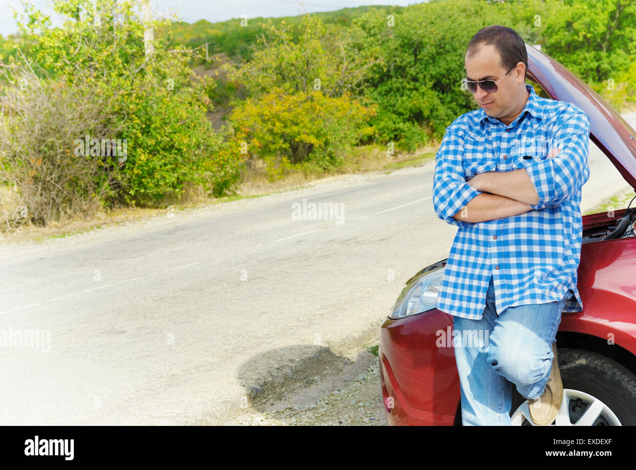 Adult man is standing near his broken car waiting for tow Stock Photo