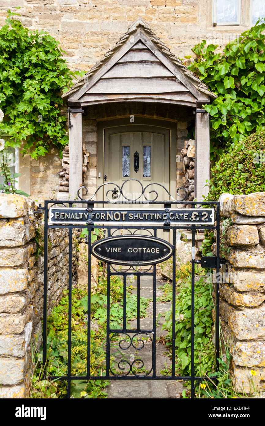 Rural English stone house 'Vine Cottage' in Cotswold village, Lower Slaughter, with wooden porch, gate and sign, Penalty for not shutting the gate £2 Stock Photo