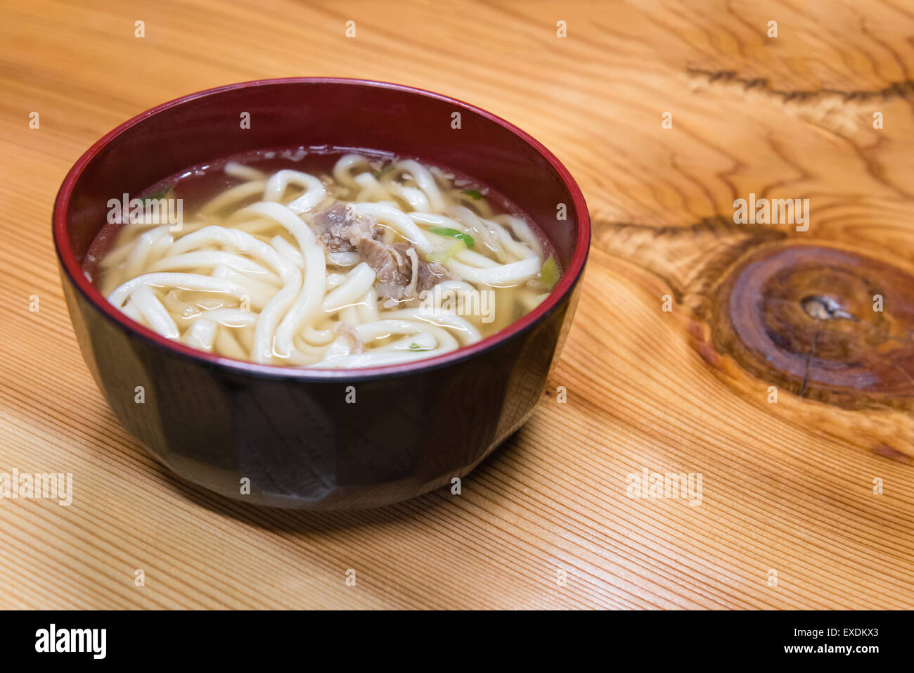 A red and black wooden bowl of Japanese udon noodles and meat. Stock Photo