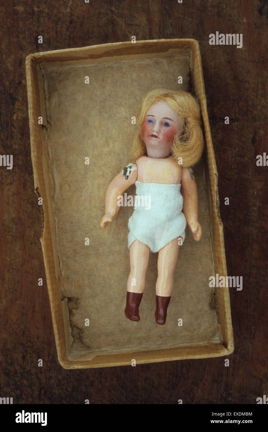 Small antique bisque doll with painted red cheeks and brown boots blonde hair and white underwear lying in box Stock Photo