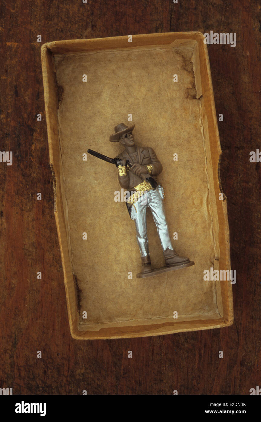Plastic model of cowboy with poorly painted silver trousers holding rifle over shoulder lying in cardboard box Stock Photo