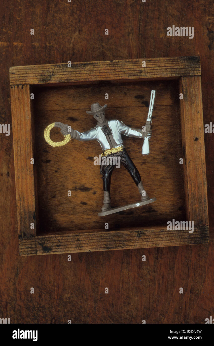 Plastic model of cowboy with poorly painted silver jacket brandishing rifle and coil of rope and standing in wooden box Stock Photo