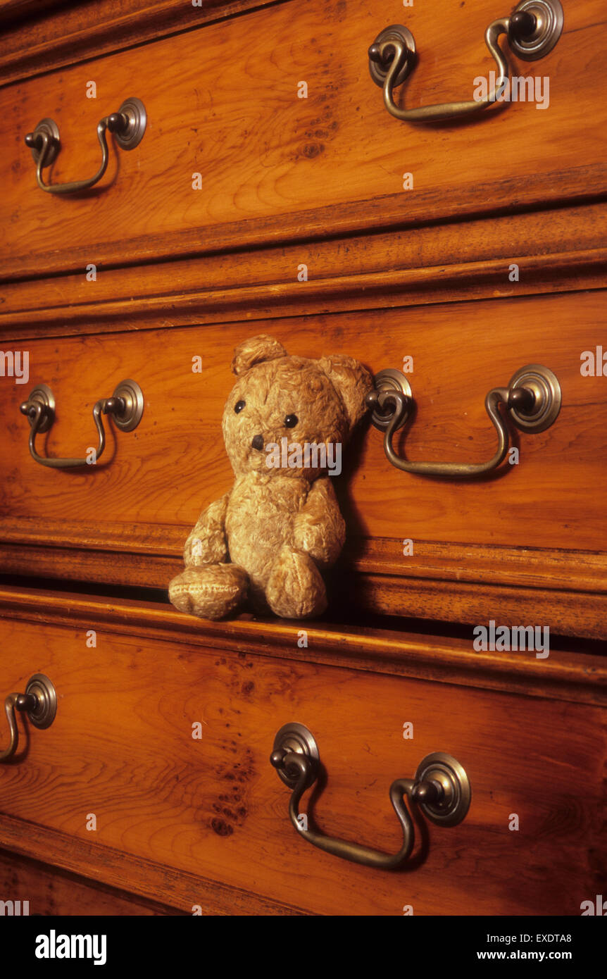 Vintage worn beige teddy bear sitting on front lip of drawer in antique chest of drawers Stock Photo
