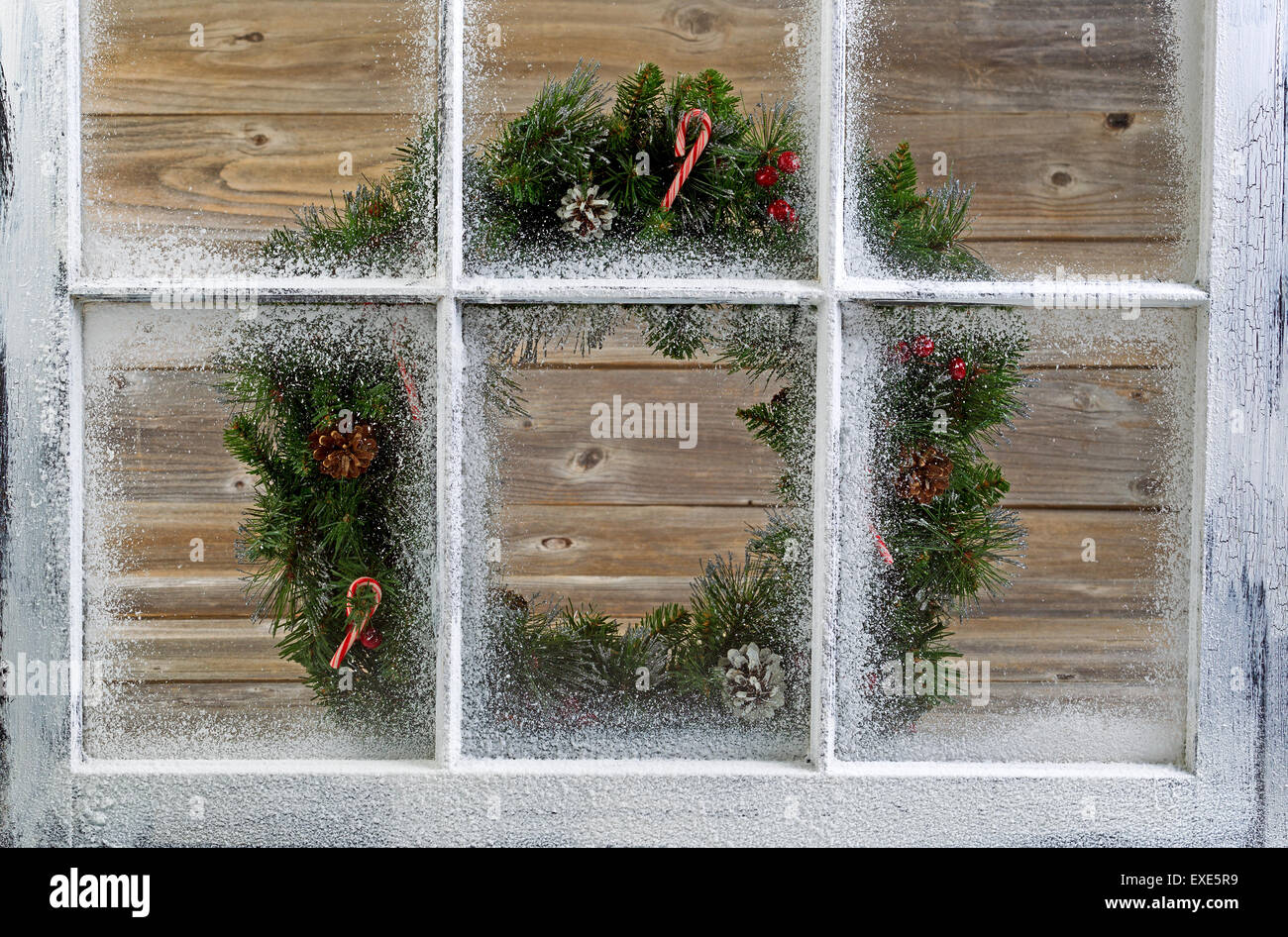 Snow covered window with decorative Christmas wreath on window with rustic wood in background. Stock Photo