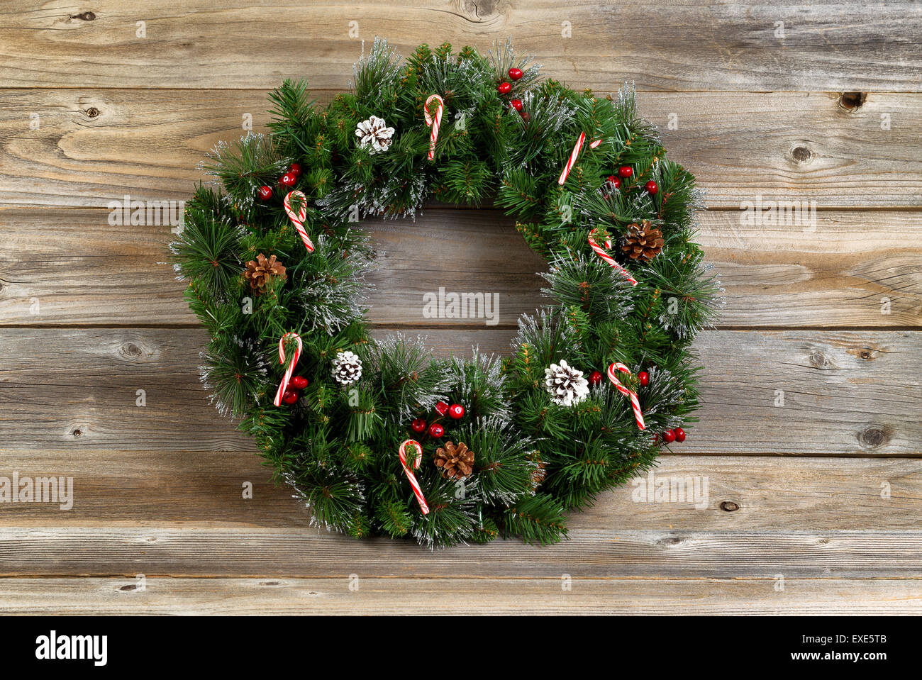 Christmas wreath decorated with pine cones, candy canes, and red berries on rustic wooden boards. Stock Photo