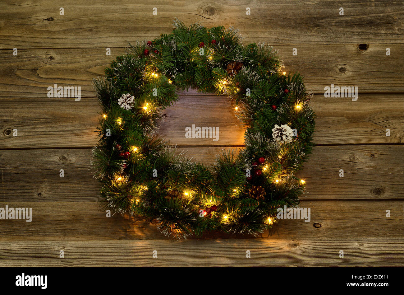 Christmas wreath with white lights on rustic wooden boards.  Low lighting to bring out glow of lights. Stock Photo
