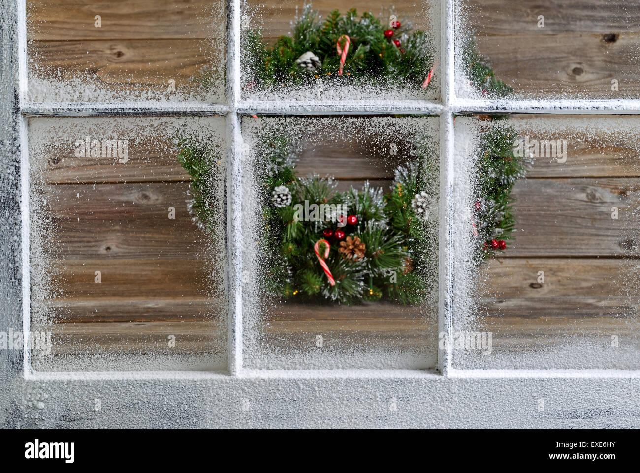Snow covered window with decorative Christmas wreath on rustic wooden boards in background. Focus on window glass and sills. Stock Photo