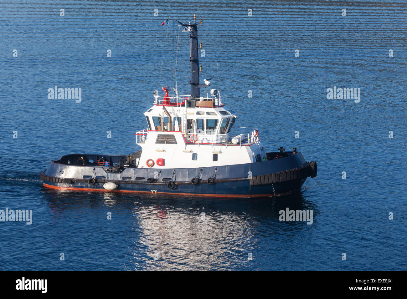 Tug boat with white superstructure and dark blue hull underway, side view Stock Photo