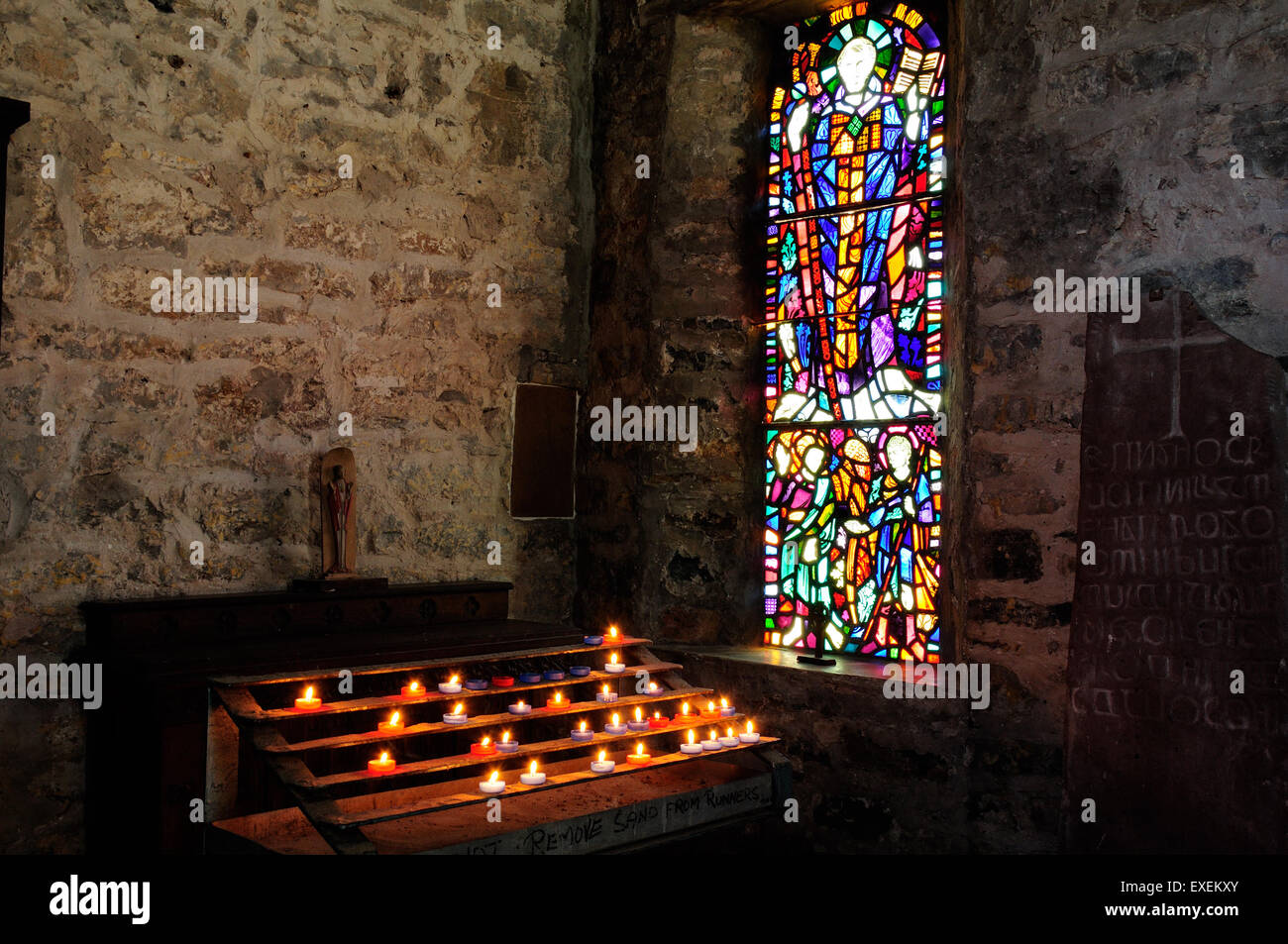 Lit candles and stained glass window St Illtyds Church The Old Priory Caldey Island Wales Stock Photo
