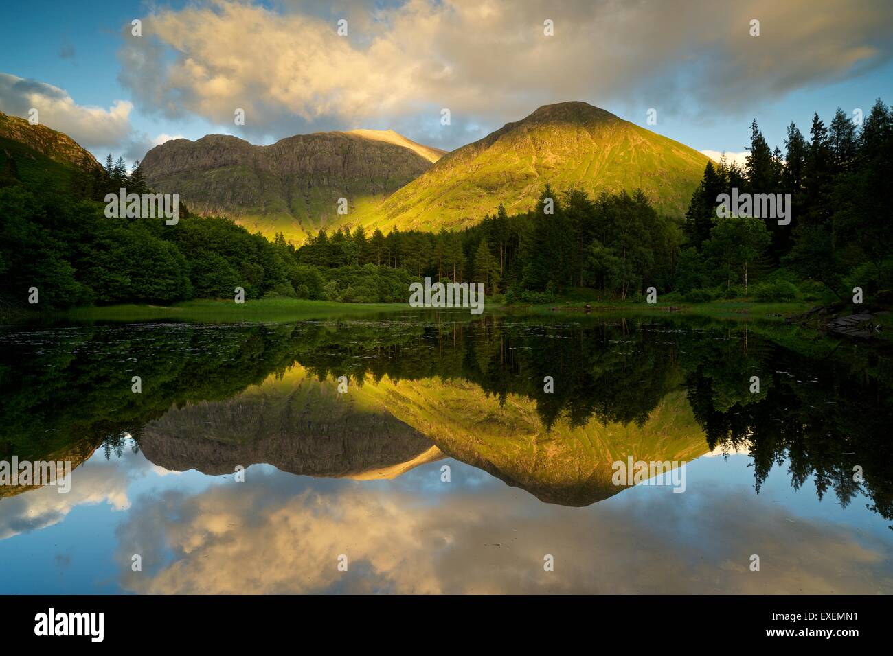 The low dipping sun casts a golden glow on the mountains of Glencoe whilst being reflected in the still Torren Loch Stock Photo