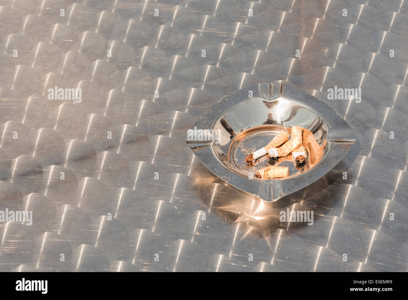 Stubbed out cigarette ends filters cigarettes in a stainless steel ashtray outdoors on a metal table. Smoking concept conceptual Stock Photo