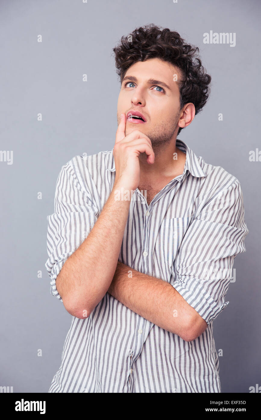 Portrait of a pensive young man standing over gray background and looking up Stock Photo