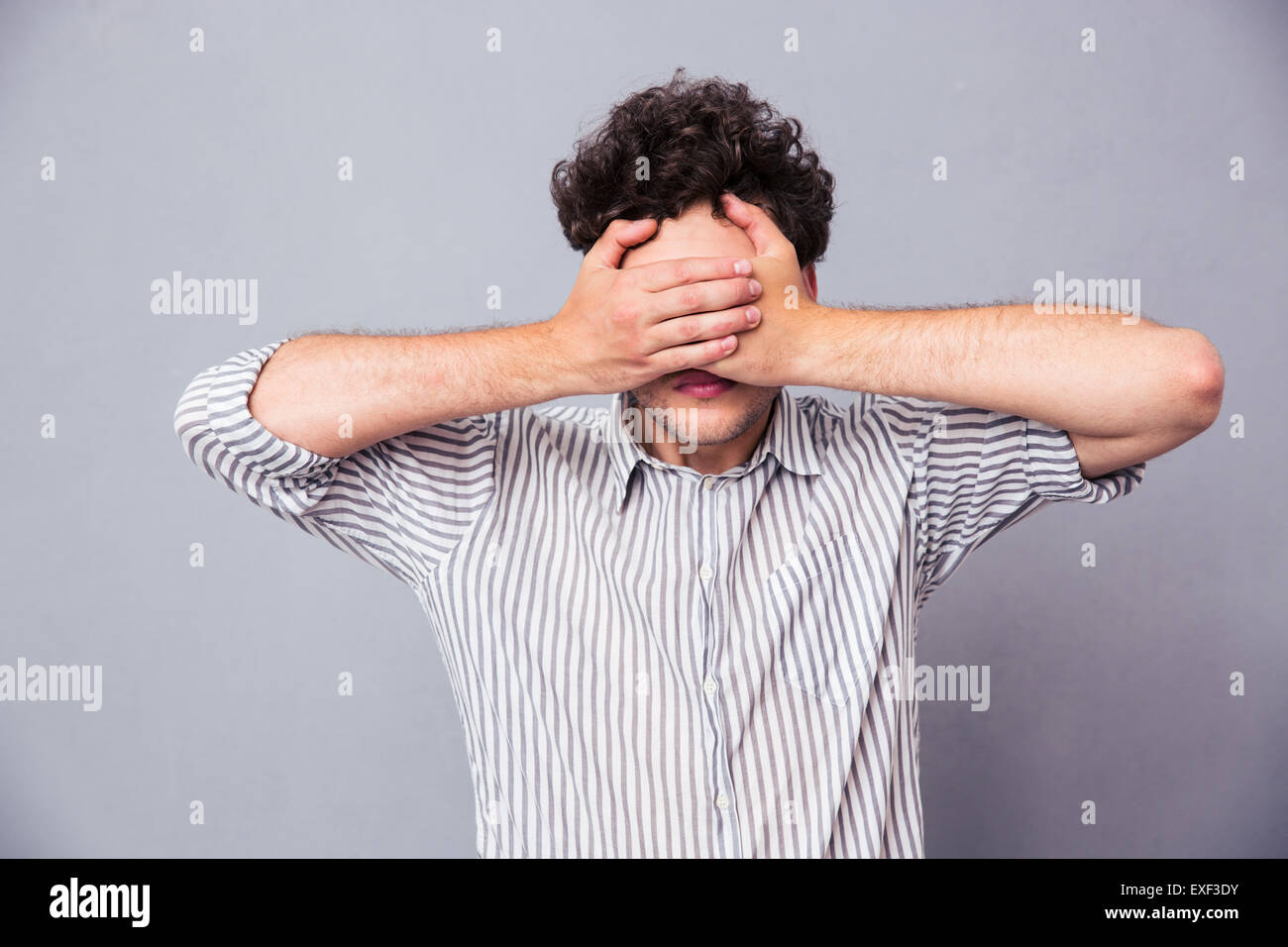 Man covering his eyes with hands over gray background Stock Photo Alamy