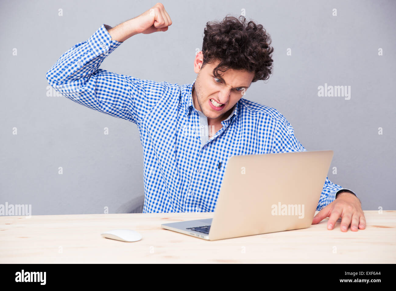Angry man sitting at the table with laptop over gray background Stock Photo