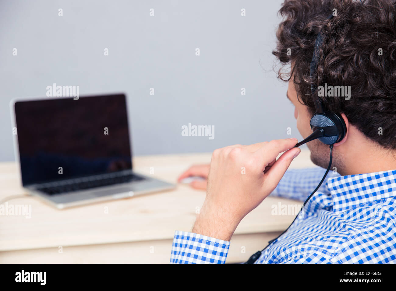 Back view portrait of a male operator with headphones looking at laptop ...