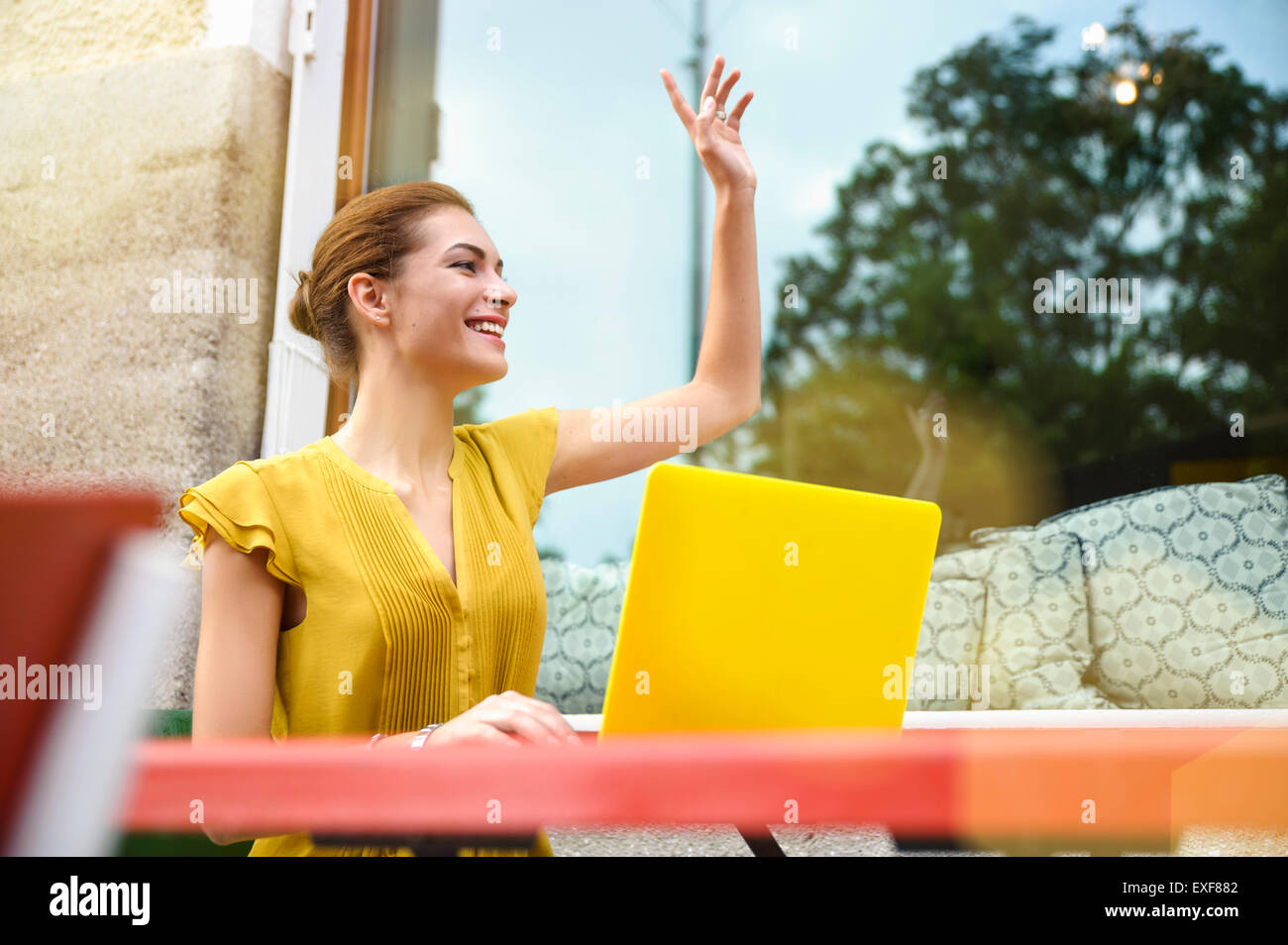 Young woman signalling to waiter, using laptop outside cafe Stock Photo
